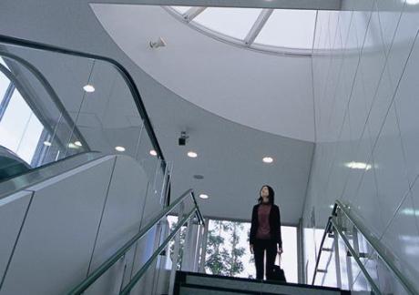 A woman at the top of the stairwell looks up at a semi-circle skylight