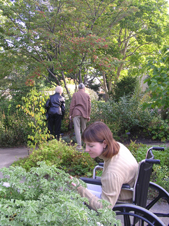 Two standing women as well as a woman in a wheelchair experiencing the garden