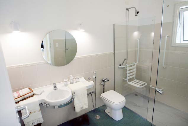 Bright bathroom with light brown tile about halfway up the walls, a glass shower with a transfer seat