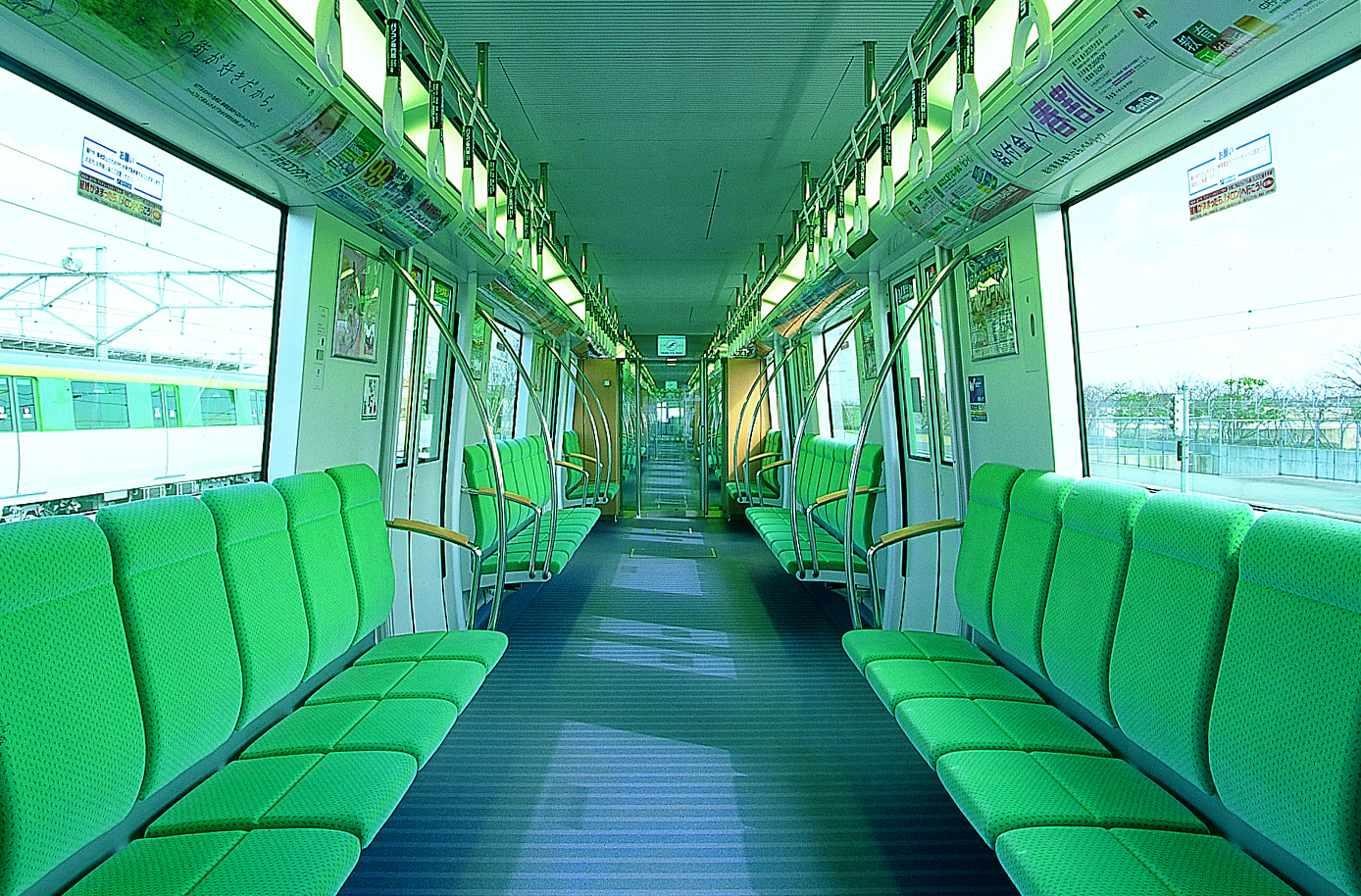 Interior of subway car with green seats along the wall and three doorways per side of car. 