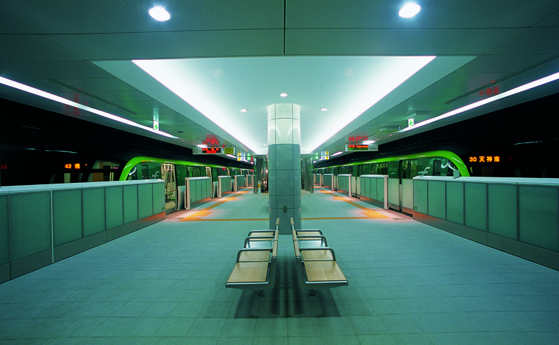 Photo of the length of the subway platform with benches and columns down the middle. Walls with sliding gates, prevent riders from falling onto the tracks.