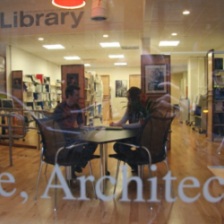 Looking through window into reading area from the street where two people are sitting at a table.