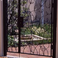 Black iron gates with stylized flowers in front of garden