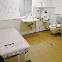 Large single user bathroom with brown tiled floor and white fixtures.